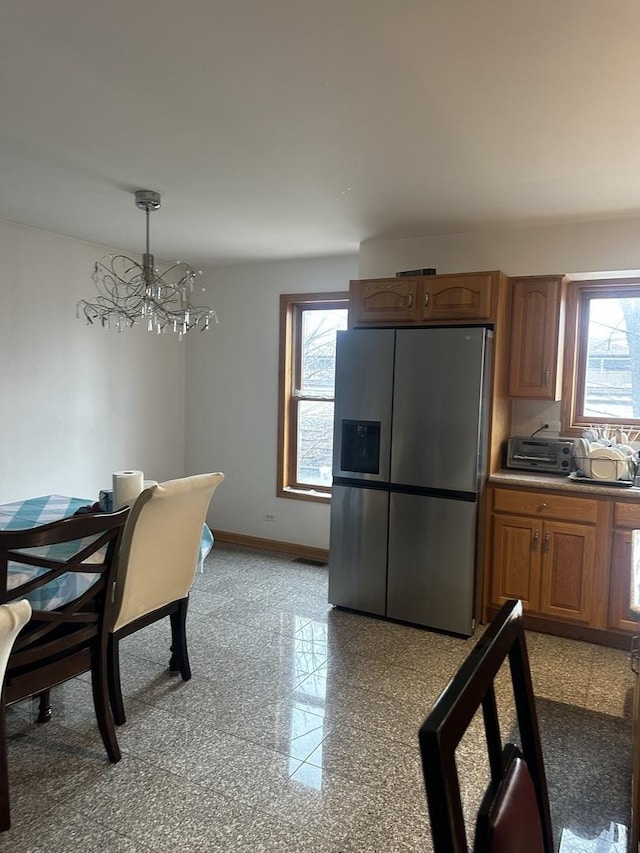 kitchen with brown cabinetry, baseboards, a chandelier, granite finish floor, and stainless steel fridge