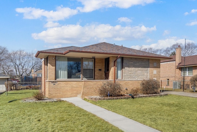 view of front of property with brick siding, a front yard, a trampoline, and fence