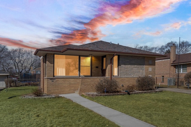 view of front of home with brick siding, a front lawn, a trampoline, fence, and central AC