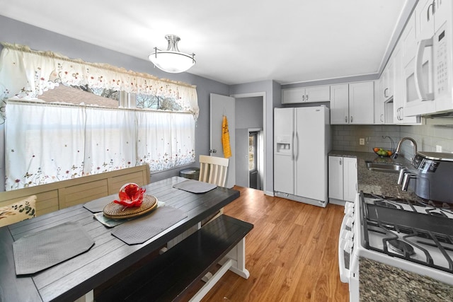 kitchen featuring light wood-style flooring, a sink, tasteful backsplash, dark stone counters, and white appliances