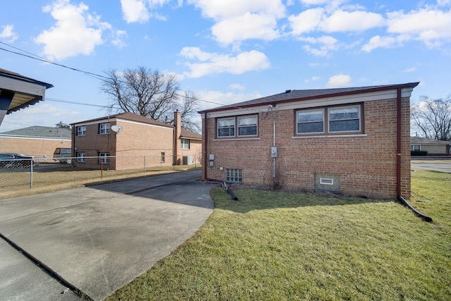 back of house featuring a lawn, concrete driveway, brick siding, and fence