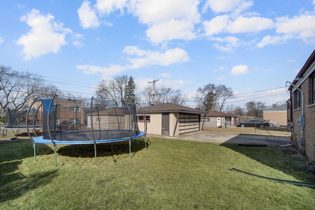 view of yard featuring a trampoline, fence, a garage, an outbuilding, and a patio