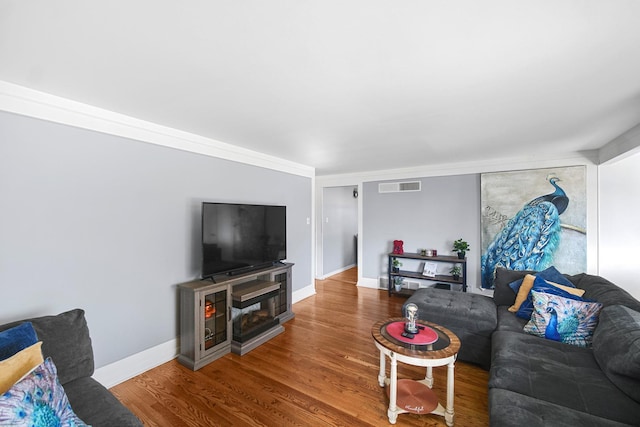 living room with visible vents, baseboards, wood finished floors, and crown molding