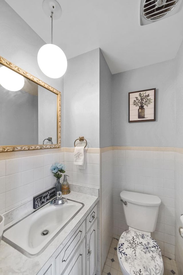 bathroom featuring visible vents, a wainscoted wall, toilet, vanity, and tile walls