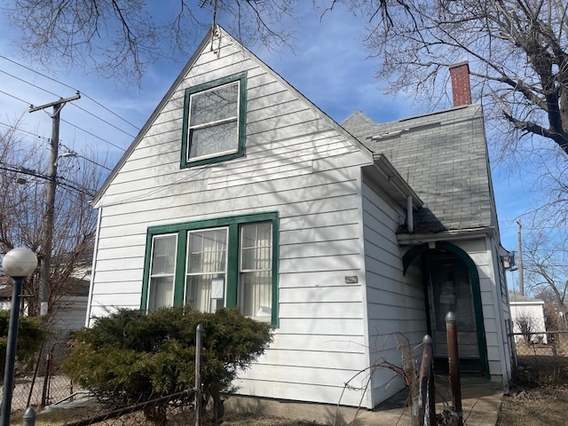 view of home's exterior with roof with shingles, a chimney, and fence