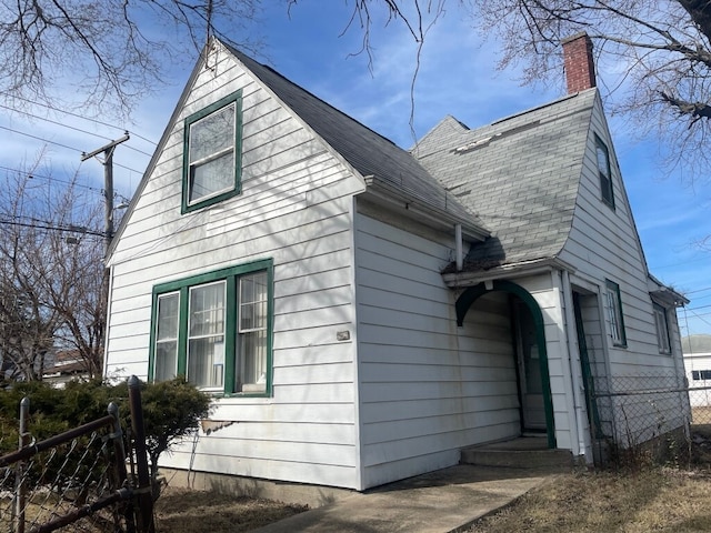 view of property exterior featuring a shingled roof, a chimney, and fence