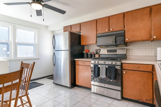 kitchen featuring brown cabinets, backsplash, appliances with stainless steel finishes, light countertops, and ceiling fan