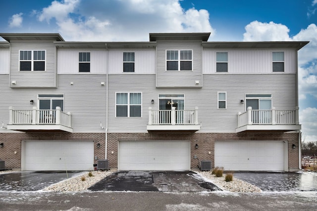 rear view of property featuring central air condition unit, brick siding, and a garage