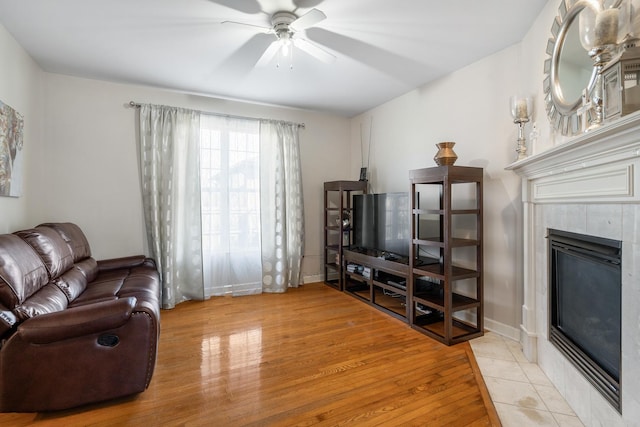 living area with baseboards, wood finished floors, a ceiling fan, and a tile fireplace