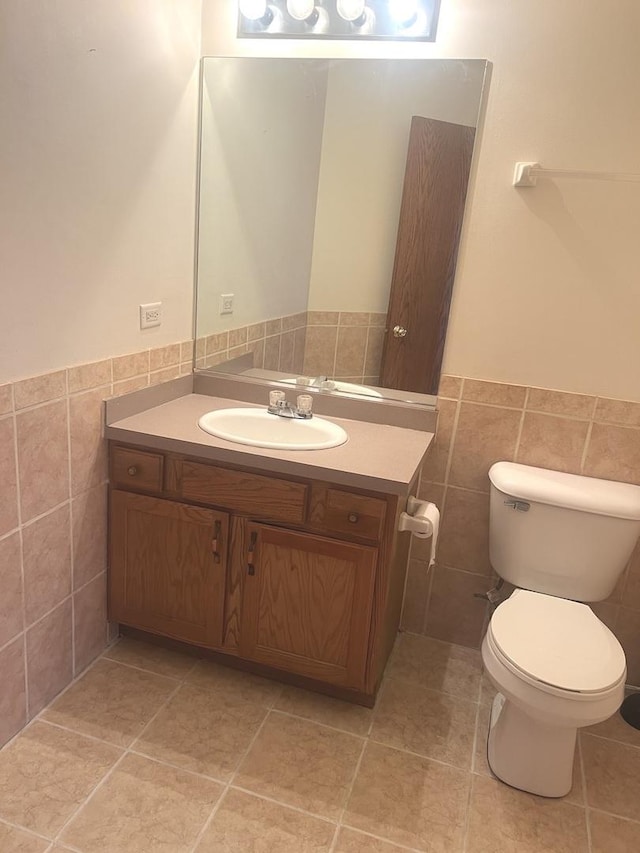 half bathroom with tile patterned floors, a wainscoted wall, toilet, tile walls, and vanity