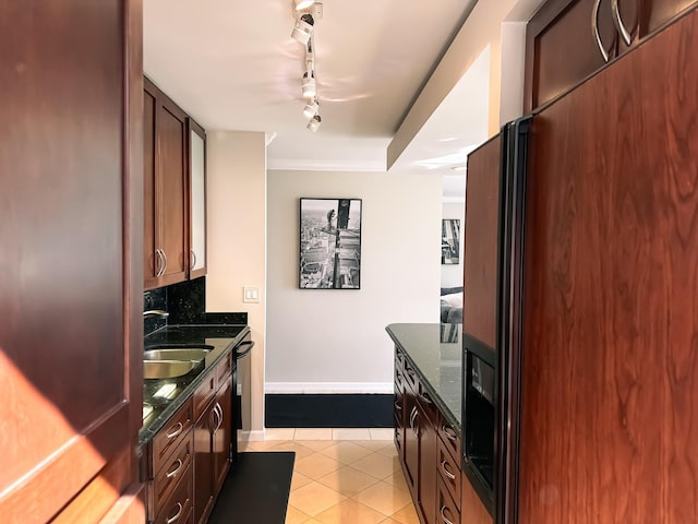 kitchen featuring light tile patterned floors, baseboards, dark stone counters, a sink, and black fridge