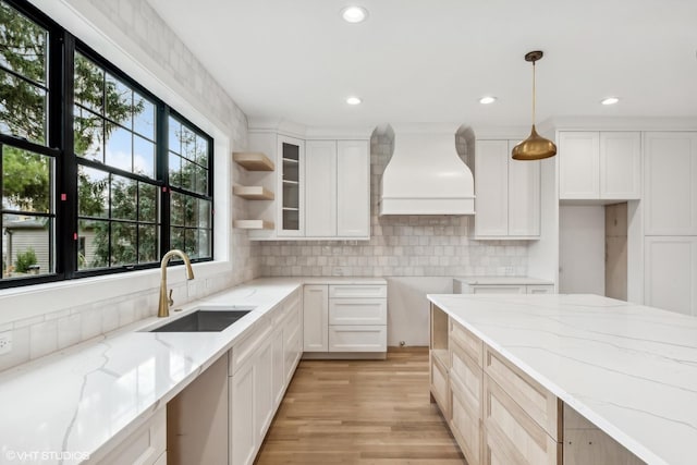 kitchen with tasteful backsplash, custom range hood, light stone counters, white cabinets, and a sink