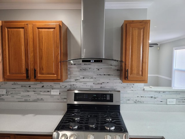 kitchen featuring brown cabinetry, stainless steel range with gas stovetop, wall chimney exhaust hood, and ornamental molding