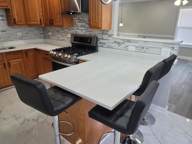 kitchen with a peninsula, stainless steel range with gas stovetop, light countertops, wall chimney exhaust hood, and marble finish floor