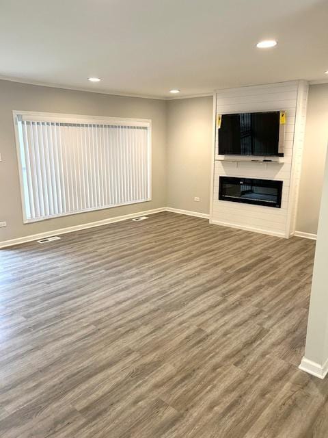 unfurnished living room with visible vents, a large fireplace, baseboards, and wood finished floors