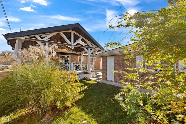 rear view of house featuring a deck, a yard, a ceiling fan, and brick siding