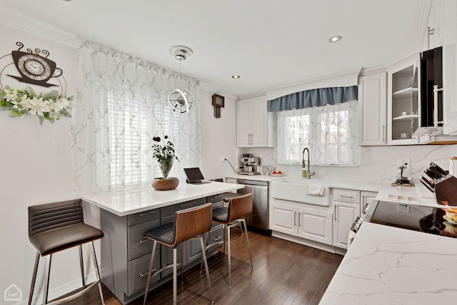 kitchen featuring a breakfast bar, a sink, stainless steel dishwasher, dark wood finished floors, and white cabinets