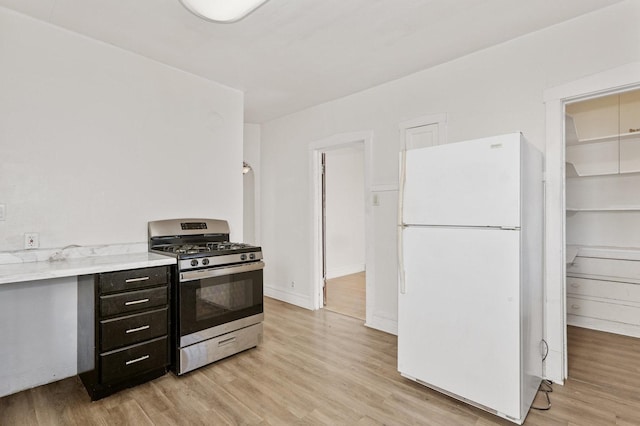 kitchen with freestanding refrigerator, gas stove, light wood-style floors, light countertops, and dark cabinets