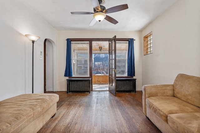 living area with arched walkways, ceiling fan, and hardwood / wood-style flooring