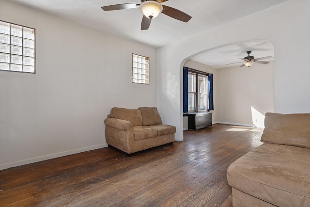 living area featuring dark wood finished floors, a ceiling fan, arched walkways, and baseboards