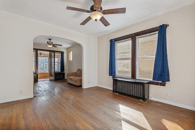 unfurnished room featuring radiator heating unit, a ceiling fan, arched walkways, and wood-type flooring