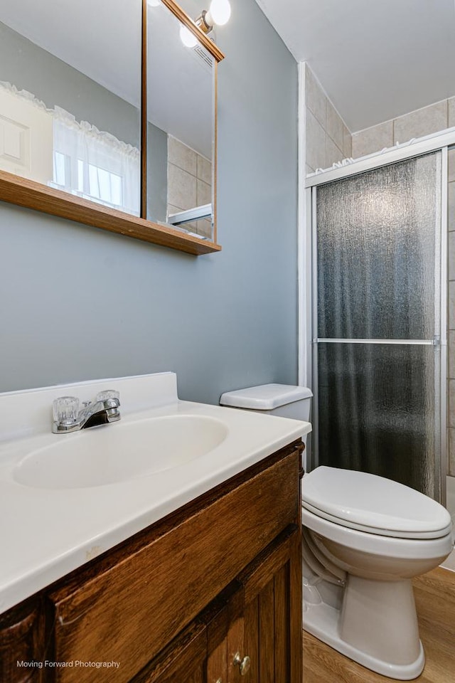 bathroom with wood finished floors, toilet, a stall shower, and vanity