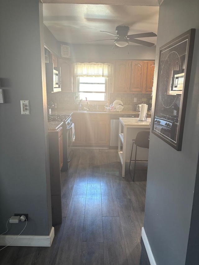 kitchen featuring stove, backsplash, ceiling fan, and dark wood-style flooring