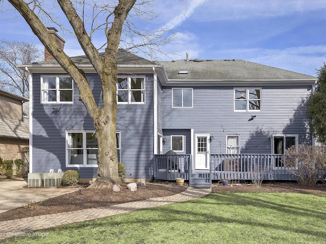 rear view of property featuring a deck, a yard, roof with shingles, and a chimney