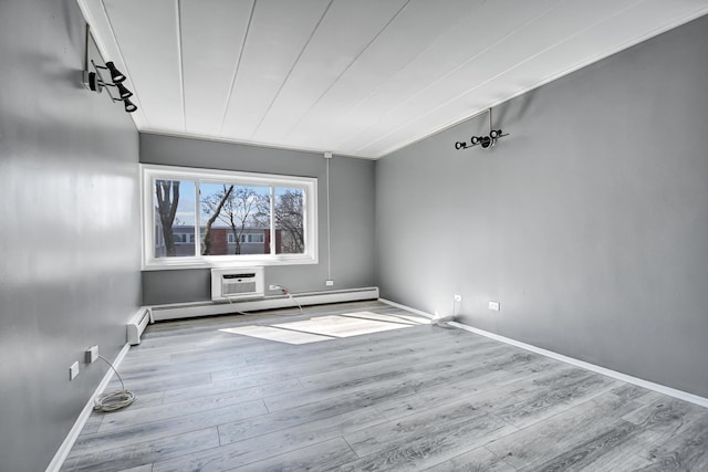 unfurnished room with a baseboard radiator, an AC wall unit, baseboards, and wood finished floors