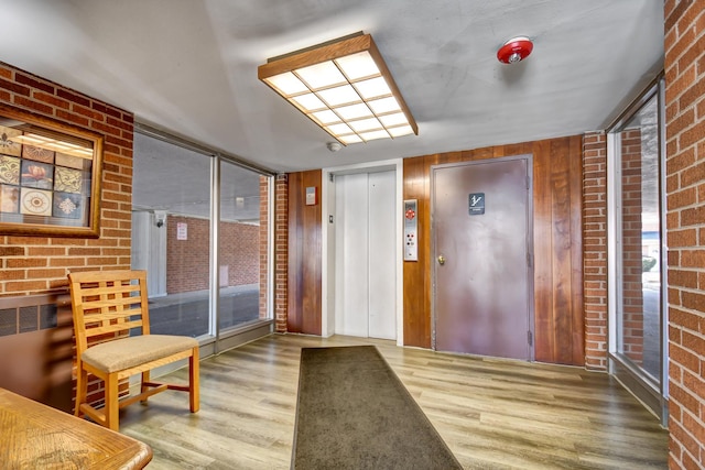 foyer featuring elevator, wood finished floors, and brick wall