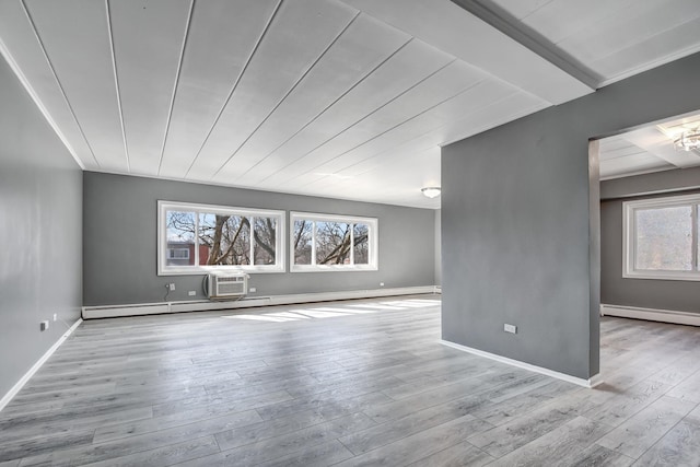 spare room featuring baseboard heating, an AC wall unit, baseboards, and wood finished floors