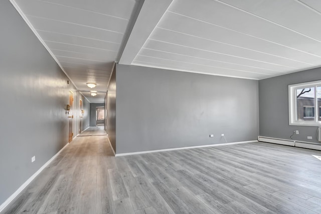 spare room featuring a baseboard heating unit, baseboards, and wood finished floors