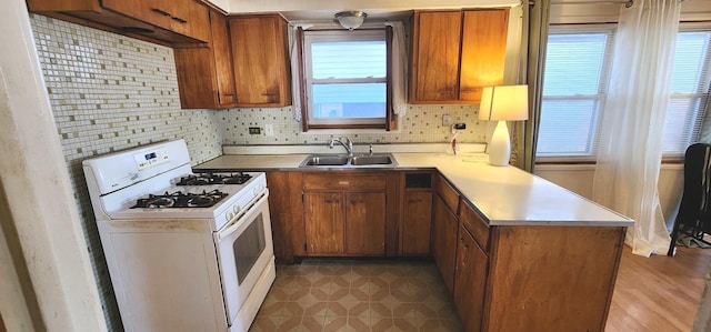 kitchen with a wealth of natural light, a sink, gas range gas stove, a peninsula, and brown cabinetry