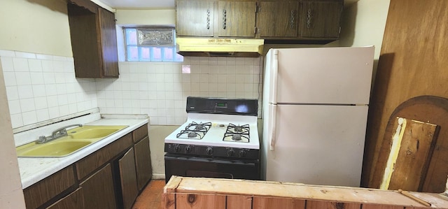 kitchen with under cabinet range hood, a sink, backsplash, freestanding refrigerator, and range with gas cooktop