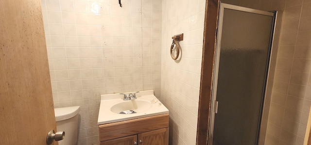 bathroom with vanity, a shower stall, toilet, and tile walls