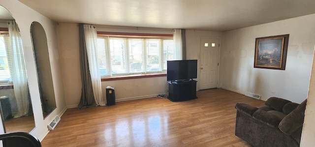 living room with visible vents, arched walkways, baseboards, and light wood-style flooring