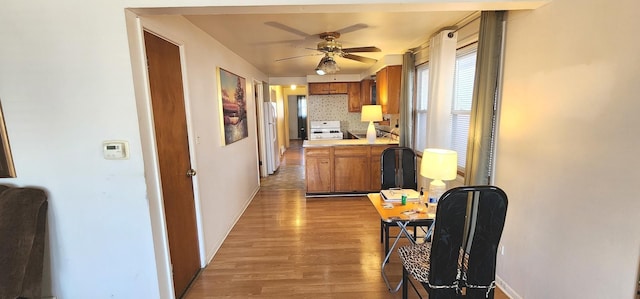 kitchen featuring stove, brown cabinets, freestanding refrigerator, and light wood-type flooring