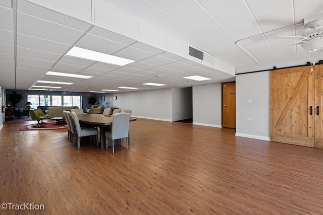 dining area featuring a drop ceiling, a barn door, visible vents, and wood finished floors