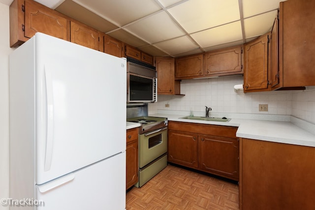 kitchen with brown cabinetry, freestanding refrigerator, a sink, decorative backsplash, and electric range oven