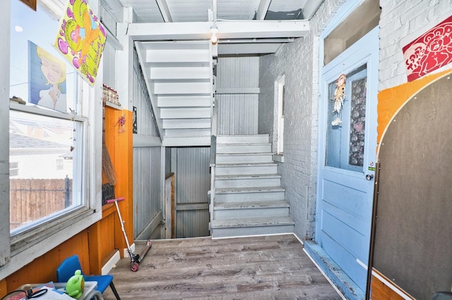 stairs with wood finished floors and brick wall