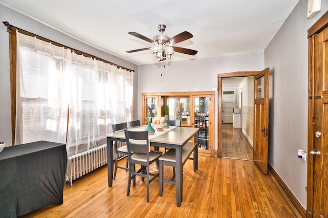 dining area with light wood-type flooring, baseboards, radiator, and ceiling fan