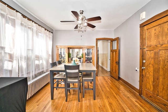 dining area with radiator heating unit, a ceiling fan, baseboards, and light wood finished floors