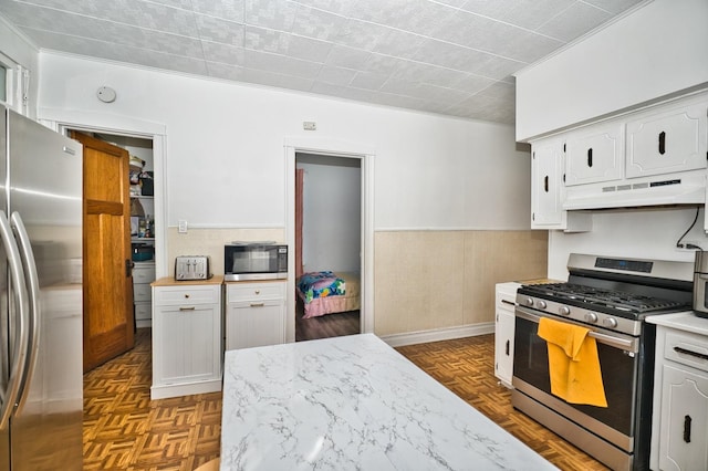 kitchen featuring a wainscoted wall, a toaster, white cabinets, under cabinet range hood, and appliances with stainless steel finishes