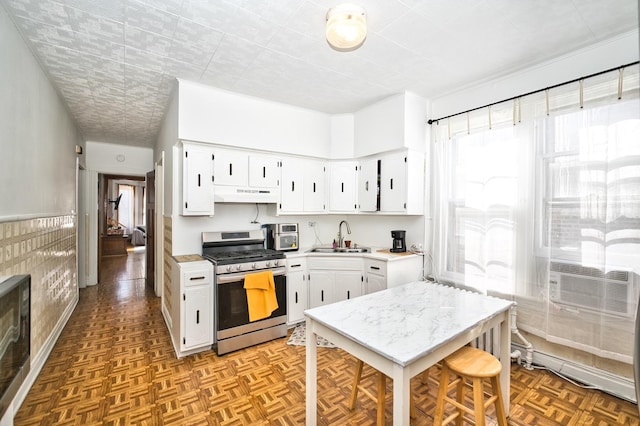 kitchen with stainless steel gas range oven, under cabinet range hood, light countertops, and a sink