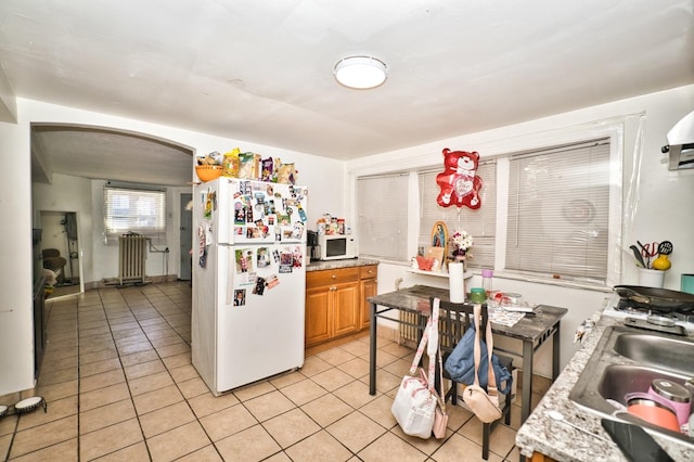 kitchen featuring light countertops, light tile patterned floors, arched walkways, white appliances, and a sink