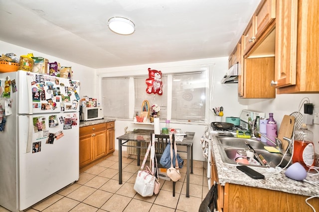 kitchen featuring under cabinet range hood, light tile patterned floors, brown cabinets, and white appliances