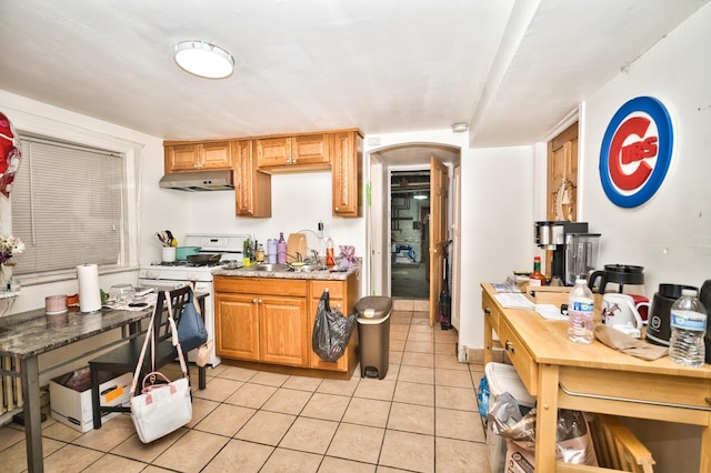 kitchen with light tile patterned floors, arched walkways, a sink, white gas range oven, and under cabinet range hood