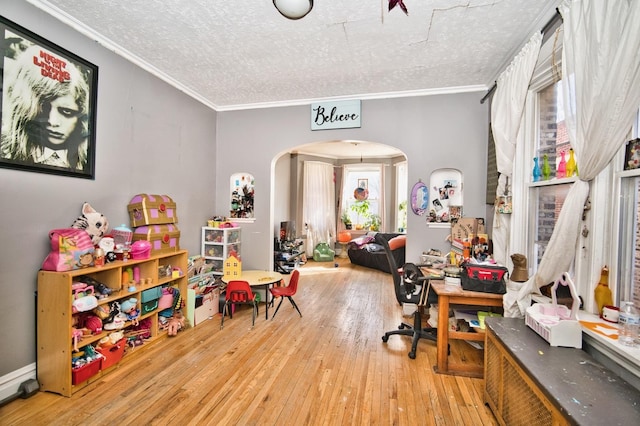 playroom with arched walkways, a textured ceiling, crown molding, and hardwood / wood-style flooring