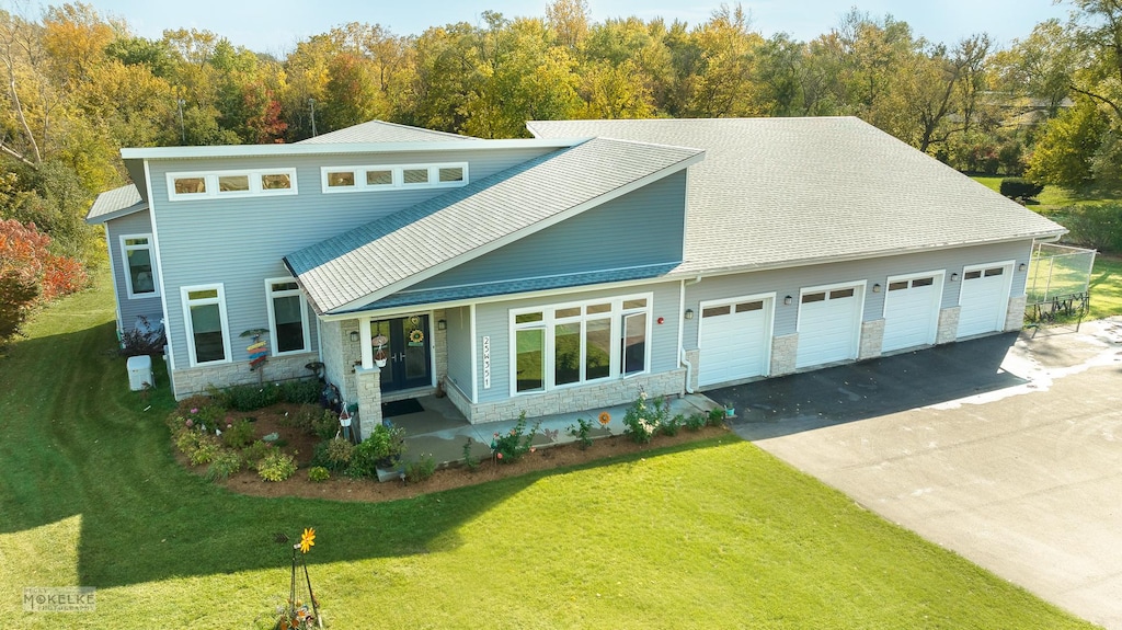 view of front of property with a front yard, roof with shingles, an attached garage, stone siding, and aphalt driveway