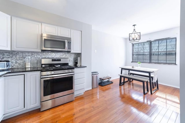 kitchen featuring a notable chandelier, tasteful backsplash, dark countertops, light wood-style floors, and appliances with stainless steel finishes